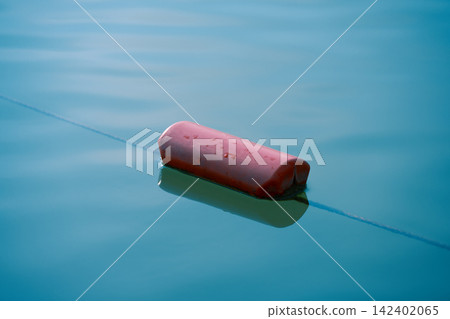 High angle shot of a red floating marker attached to a safety rope line. Clean and empty water surface with a soft reflection and large copy space for text, perfect for commercial design banners. High angle shot of a red floating marker attached to a safety rope line. Clean and empty water surface with a soft reflection and large copy space for text, perfect for commercial design banners. 142402065