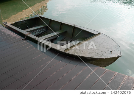 Beautiful professional stock photography of a single rowboat floating near a pier during a summer day. Concept of lake recreation, boating adventures, country weekend, and freedom. Beautiful professional stock photography of a single rowboat floating near a pier during a summer day. Concept of lake recreation, boating adventures, country weekend, and freedom. 142402076