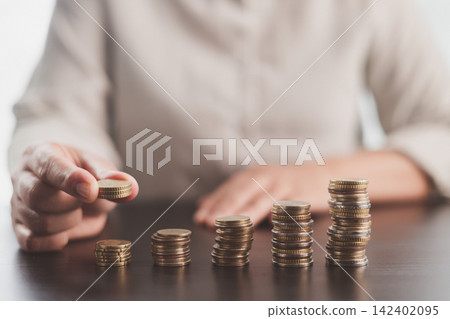 Person adding coins to rising stacks represents consistent saving, investment growth, financial progress, wealth building, budgeting discipline, compound returns, and long-term economic success. Person adding coins to rising stacks represents consistent saving, investment growth, financial progress, wealth building, budgeting discipline, compound returns, and long-term economic success. 142402095