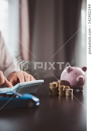 Calculator, piggy bank, stacked coins, and blue car model depict vehicle budgeting, saving for transportation, auto purchase planning, financing decisions, household expenses, and future goals. Calculator, piggy bank, stacked coins, and blue car model depict vehicle budgeting, saving for transportation, auto purchase planning, financing decisions, household expenses, and future goals. 142402244
