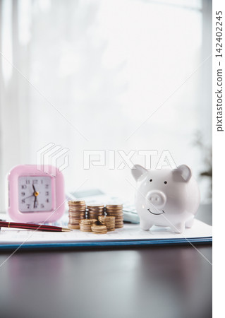 Pink clock, white piggy bank, stacked coins, calculator, and planning sheet illustrate time-based savings, household budgeting, financial discipline, goal setting, and money management. Pink clock, white piggy bank, stacked coins, calculator, and planning sheet illustrate time-based savings, household budgeting, financial discipline, goal setting, and money management. 142402245