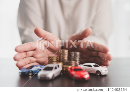 Hands protecting multiple model cars and stacked coins symbolize fleet insurance, vehicle coverage, asset protection, financial security, risk management, and responsible ownership planning. Hands protecting multiple model cars and stacked coins symbolize fleet insurance, vehicle coverage, asset protection, financial security, risk management, and responsible ownership planning. 142402264