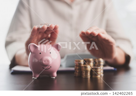 Hands protecting a pink piggy bank and stacked coins, symbolizing savings security, risk management, emergency funds, household budgeting, financial care, wealth protection, and future stability. Hands protecting a pink piggy bank and stacked coins, symbolizing savings security, risk management, emergency funds, household budgeting, financial care, wealth protection, and future stability. 142402265