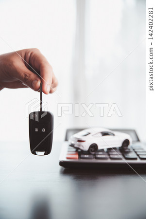 Hand holding a car key beside a white vehicle model on a calculator symbolizes auto purchase approval, financing access, loan agreement, payment planning, ownership, and dealership transactions. Hand holding a car key beside a white vehicle model on a calculator symbolizes auto purchase approval, financing access, loan agreement, payment planning, ownership, and dealership transactions. 142402281