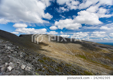 Rugged rocky slopes of Mount Aikuainvenchorr in the Khibiny Mountains near Kirovsk, Murmansk Region, Russia. Barren high-altitude terrain, weathered rocks and distant mountain ridges under a dramatic Rugged rocky slopes of Mount Aikuainvenchorr in the Khibiny Mountains near Kirovsk, Murmansk Region, Russia. Barren high-altitude terrain, weathered rocks and distant mountain ridges under a dramatic 142402305