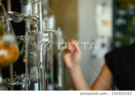 Scientist Collecting Essential Oil Drop from Glass Distillation Apparatus in Laboratory Scientist Collecting Essential Oil Drop from Glass Distillation Apparatus in Laboratory 142402383