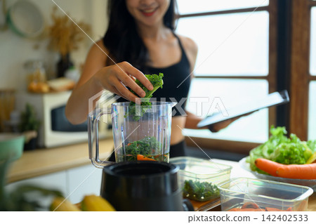 Young Woman Adding Kale to Blender for Healthy Green Smoothie in Home Kitchen Young Woman Adding Kale to Blender for Healthy Green Smoothie in Home Kitchen 142402533