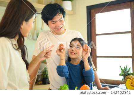 Happy Family Cooking Together in Kitchen, Parents and Daughter Holding Eggs While Preparing Healthy Meal at Home 142402541