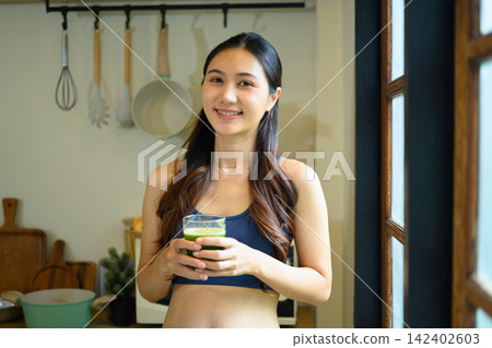 Young Woman in Sports Bra Holding Green Kale Smoothie in Kitchen, Healthy Lifestyle Wellness Concept Young Woman in Sports Bra Holding Green Kale Smoothie in Kitchen, Healthy Lifestyle Wellness Concept 142402603