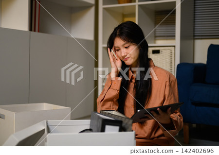 Young Asian Woman Packing Personal Belongings in Office Box After Job Loss, Looking Sad and Thoughtful Young Asian Woman Packing Personal Belongings in Office Box After Job Loss, Looking Sad and Thoughtful 142402696