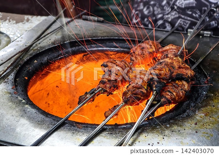 Skewers of grilled meat cooking in spicy sauce on stove Skewers of grilled meat cooking in spicy sauce on stove 142403070