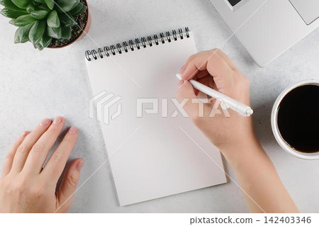 Person writing in notebook with coffee and plants on desk Person writing in notebook with coffee and plants on desk 142403346