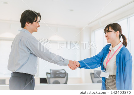Office scene: Male and female employees exchanging smiles and handshakes. Office scene: Male and female employees exchanging smiles and handshakes. 142403870