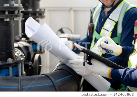 Closeup team man engineer inspecting industrial pipes looking blueprint and tablet on rooftop. Closeup team man engineer inspecting industrial pipes looking blueprint and tablet on rooftop. 142403968
