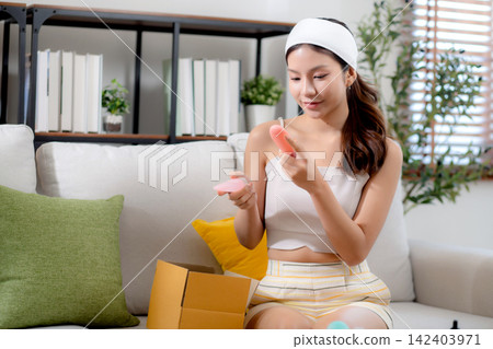 Young asian woman sitting on sofa choice cosmetic cream or lotion with shopping online. 142403971