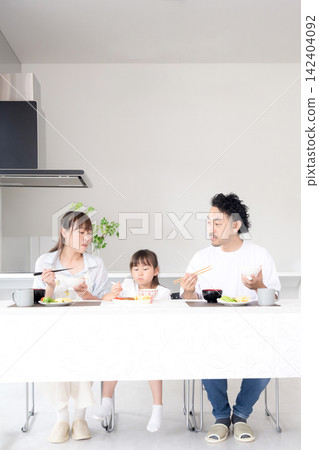 A family of three, a parent and child, sitting together happily in the dining room and beginning a meal, with smiles on their faces. This image evokes thoughts of food education and happy family gatherings. A family of three, a parent and child, sitting together happily in the dining room and beginning a meal, with smiles on their faces. This image evokes thoughts of food education and happy family gatherings. 142404092