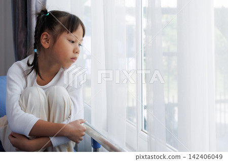 Sad little Asian girl hugging her knees while sitting on hospital bed. Lonely Sick mental health child pediatric patient in hospital room. Sad little Asian girl hugging her knees while sitting on hospital bed. Lonely Sick mental health child pediatric patient in hospital room. 142406049