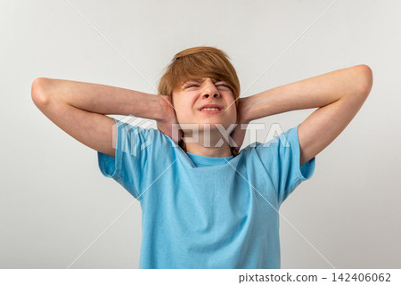 Young boy experiencing discomfort and annoyance, covering his ears with hands to block out unpleasant, excessive sound and showing an expression of irritation 142406062