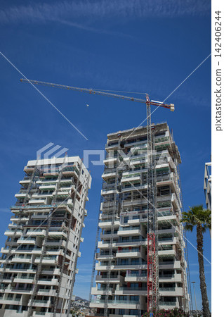 Tall red construction crane builds modern residential glass skyscrapers in an urban setting Tall red construction crane builds modern residential glass skyscrapers in an urban setting 142406244