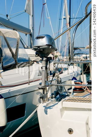 Outboard motor mounted on a sailboat stern inside a modern marina. Concept of marine transport, navigation, maintenance and travel Outboard motor mounted on a sailboat stern inside a modern marina. Concept of marine transport, navigation, maintenance and travel 142406439