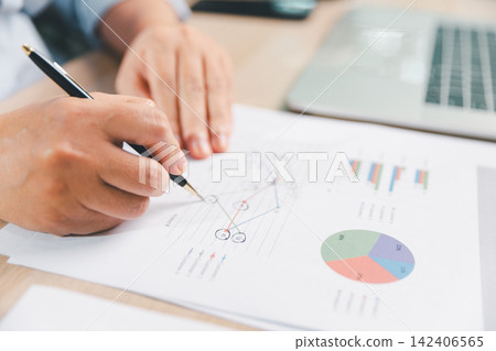 Business professional analyzing a printed line graph with pen beside a laptop, representing data analysis, performance tracking, financial planning, strategy, and informed decision making at work. Business professional analyzing a printed line graph with pen beside a laptop, representing data analysis, performance tracking, financial planning, strategy, and informed decision making at work. 142406565