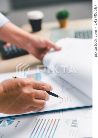 Business professional reviewing and turning printed report pages with a pen beside a laptop, representing document checking, data analysis, audit review, administration, Business professional reviewing and turning printed report pages with a pen beside a laptop, representing document checking, data analysis, audit review, administration, 142406567