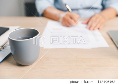Ceramic mug on office desk with blurred business professional writing notes in background, representing workplace productivity, planning, paperwork, focus, morning routine, Ceramic mug on office desk with blurred business professional writing notes in background, representing workplace productivity, planning, paperwork, focus, morning routine, 142406568