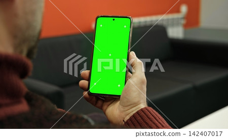 Over the shoulder view of man holding smartphone vertically with green screen chroma key and tracking markers. Male user looking at mobile phone template mockup blank display for app design tracking Over the shoulder view of man holding smartphone vertically with green screen chroma key and tracking markers. Male user looking at mobile phone template mockup blank display for app design tracking 142407017