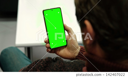 Man holding smartphone with green screen and tracking markers close up over shoulder view. Mobile phone mockup display chroma key space for application web template. Digital device usage Man holding smartphone with green screen and tracking markers close up over shoulder view. Mobile phone mockup display chroma key space for application web template. Digital device usage 142407022
