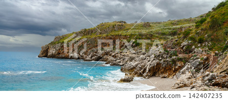 picturesque panorama of a rocky cliff face meeting the vibrant blue sea, with a wooden staircase leading up the grassy hillside picturesque panorama of a rocky cliff face meeting the vibrant blue sea, with a wooden staircase leading up the grassy hillside 142407235