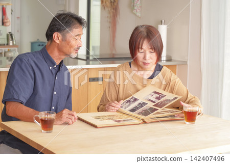 A middle-aged couple reminiscing while looking at old photographs. A middle-aged couple reminiscing while looking at old photographs. 142407496