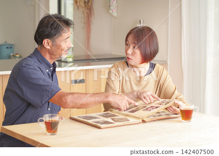 A middle-aged couple reminiscing while looking at old photographs. A middle-aged couple reminiscing while looking at old photographs. 142407500