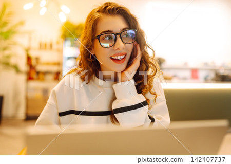 Portrait of a young woman sitting in a cafe at a laptop, working online, freelancing. Technologies. Portrait of a young woman sitting in a cafe at a laptop, working online, freelancing. Technologies. 142407737