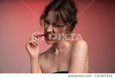 Woman biting a red chili pepper showing a spicy, hot, and provocative expression with a hungry feeling Woman biting a red chili pepper showing a spicy, hot, and provocative expression with a hungry feeling 142407819
