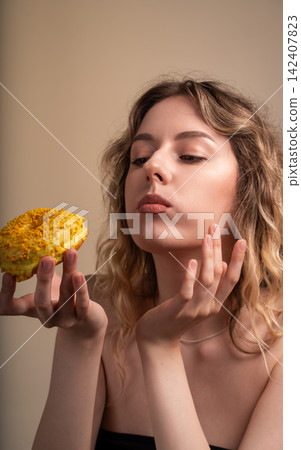 Young woman contemplating a delicious treat, holding a yellow glazed donut with sprinkles. Focusing on craving and sweet food Young woman contemplating a delicious treat, holding a yellow glazed donut with sprinkles. Focusing on craving and sweet food 142407823