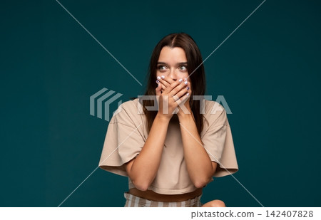 Young woman covering mouth with hands, feeling fear, expressing shock, keeping a secret, feeling afraid to speak Young woman covering mouth with hands, feeling fear, expressing shock, keeping a secret, feeling afraid to speak 142407828