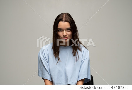 Young woman subtly smiling with a skeptical expression, looking directly at camera in a studio portrait Young woman subtly smiling with a skeptical expression, looking directly at camera in a studio portrait 142407833