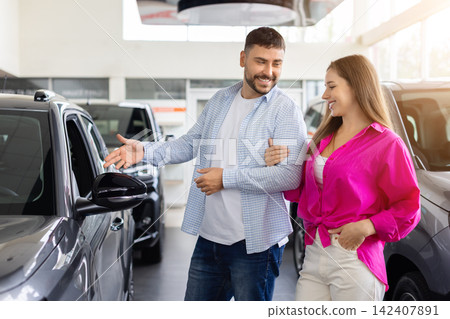 Young couple examining new car together in dealership showroom Young couple examining new car together in dealership showroom 142407891