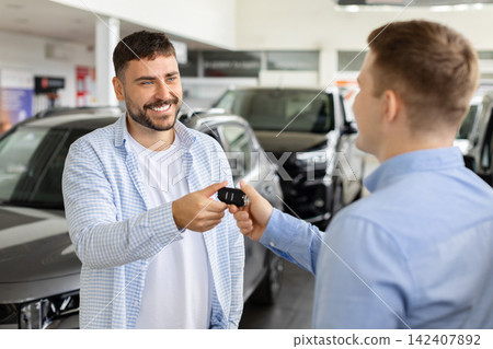 Male buyer receiving car keys from sales consultant inside modern dealership showroom Male buyer receiving car keys from sales consultant inside modern dealership showroom 142407892