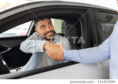 Male buyer shaking hands with car sales consultant through open vehicle window Male buyer shaking hands with car sales consultant through open vehicle window 142407894