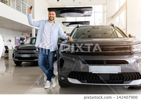 Buyer holding car keys while standing beside new vehicle in dealership showroom Buyer holding car keys while standing beside new vehicle in dealership showroom 142407900