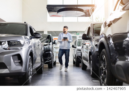 Young male customer walking through modern car dealership with tablet Young male customer walking through modern car dealership with tablet 142407905