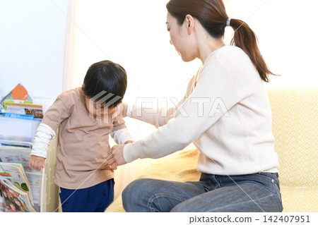 An Asian mother helping her child get dressed. An Asian mother helping her child get dressed. 142407951
