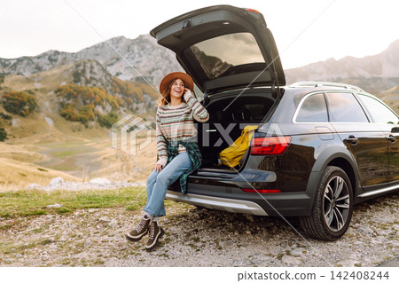 Young woman enjoying autumn nature while sitting in the trunk of her car during a trip. Road trip. Young woman enjoying autumn nature while sitting in the trunk of her car during a trip. Road trip. 142408244