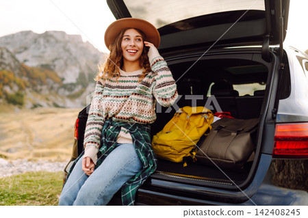 Young woman enjoying autumn nature while sitting in the trunk of her car during a trip. Road trip. 142408245