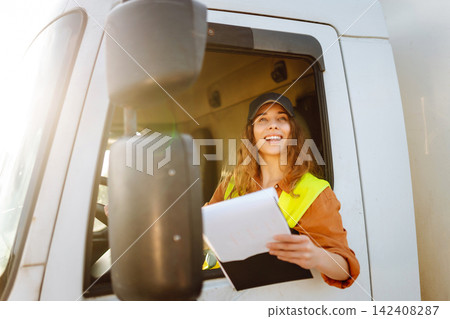 Woman truck driver steering wheel inside lorry cabin with clipboard. People and transportation Woman truck driver steering wheel inside lorry cabin with clipboard. People and transportation 142408287