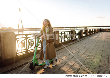 Happy woman driving electric scooter through city. Active life. Ecological transportation concept. Happy woman driving electric scooter through city. Active life. Ecological transportation concept. 142408357