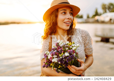 Happy woman in dress sitting on wooden pier near pond and clutched bouquet. Rustic style of wedding. Happy woman in dress sitting on wooden pier near pond and clutched bouquet. Rustic style of wedding. 142408429