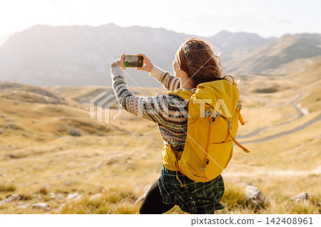 A young woman captures a moment while hiking in a mountainous landscape during golden hour A young woman captures a moment while hiking in a mountainous landscape during golden hour 142408961