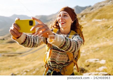 A young woman captures a moment while hiking in a mountainous landscape during golden hour A young woman captures a moment while hiking in a mountainous landscape during golden hour 142408963